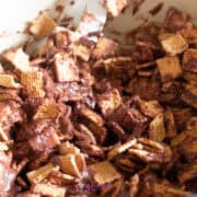 Close-up of cereal squares mixed with melted chocolate in a bowl.