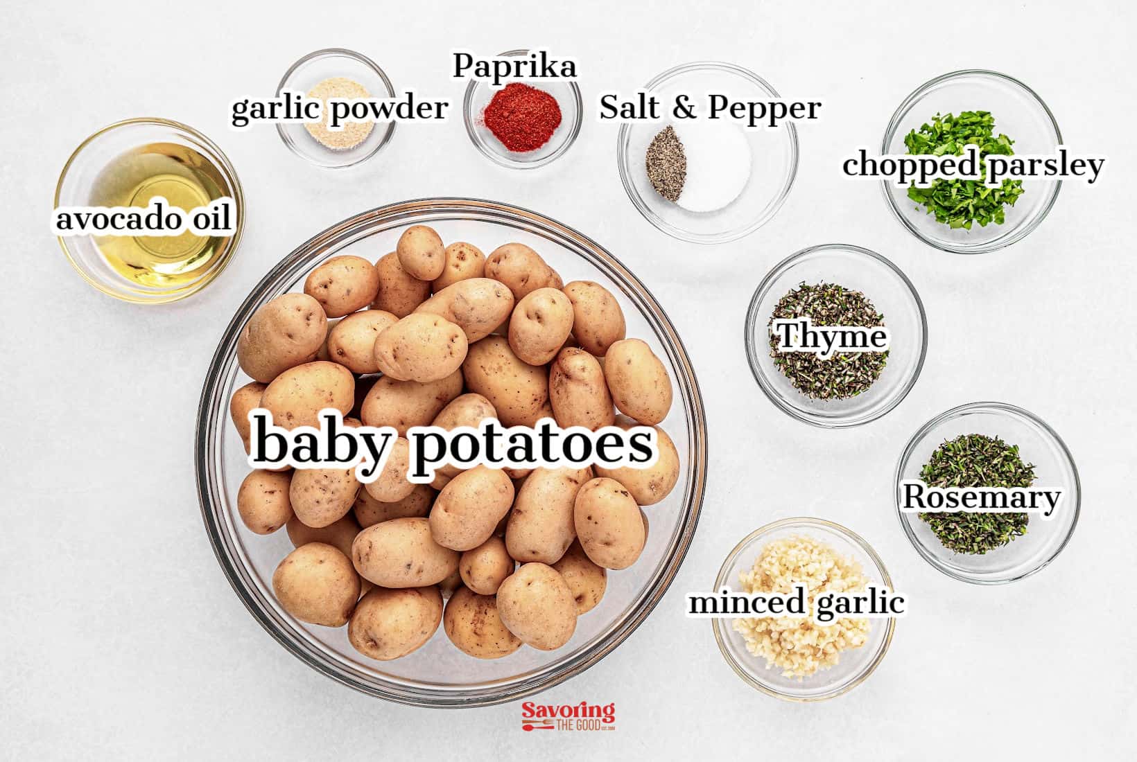 A bowl of roasted baby potatoes is surrounded by small bowls of various spices and herbs, including garlic powder, paprika, salt and pepper, chopped parsley, thyme, minced garlic, rosemary, and avocado oil.