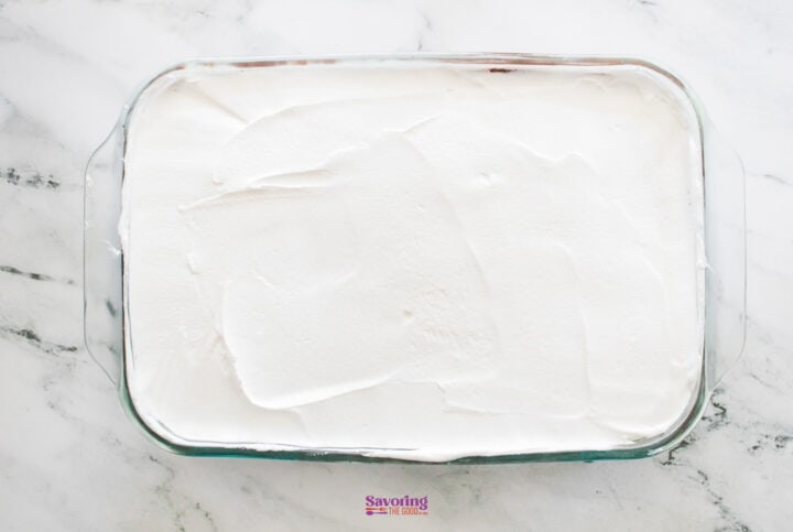 A rectangular glass dish filled with chocolate lasagna sits enticingly on the marble countertop, its top adorned with a layer of smooth white frosting.