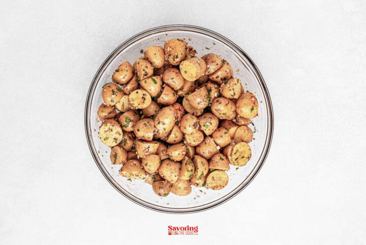 A glass bowl filled with roasted baby potatoes, seasoned to perfection and garnished with fresh herbs.