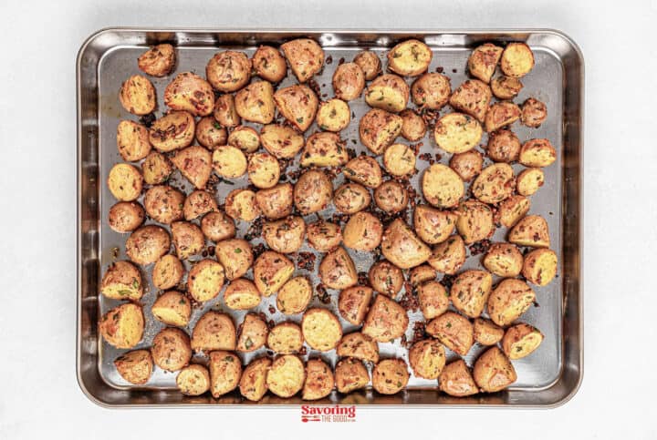 Roasted baby potato halves seasoned with herbs on a baking tray.