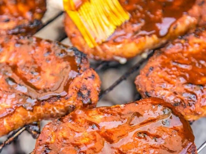 Grilling Kansas City pork chops brushed with sauce, with a yellow brush, on a grill.
