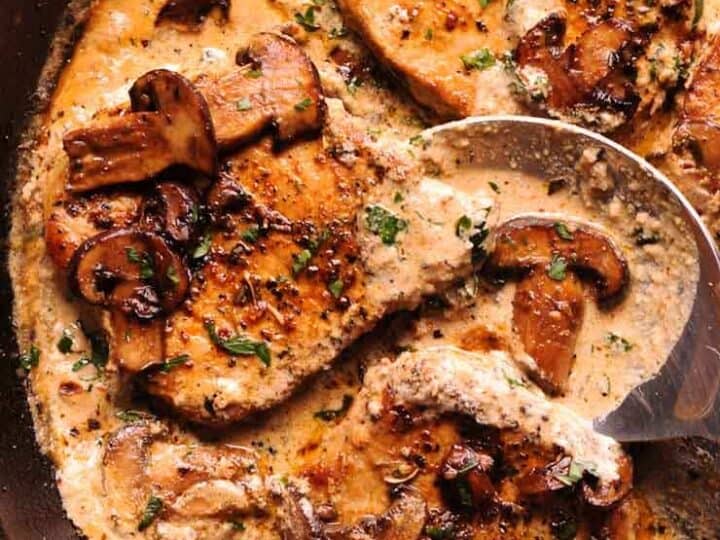 Pan-seared chicken breasts in creamy mushroom sauce, garnished with herbs in a skillet.