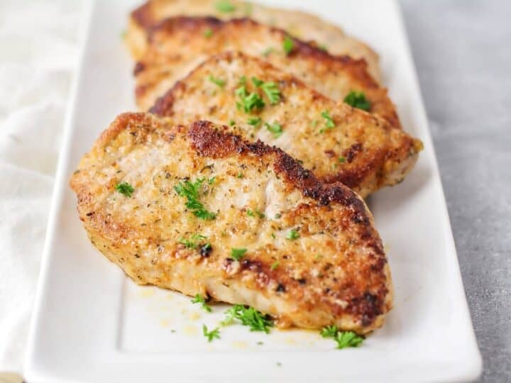 Three cooked pork chops garnished with parsley on a rectangular white plate.