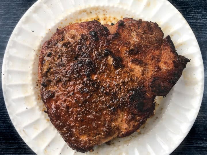 A cooked pork chop on a white plate against a dark surface.