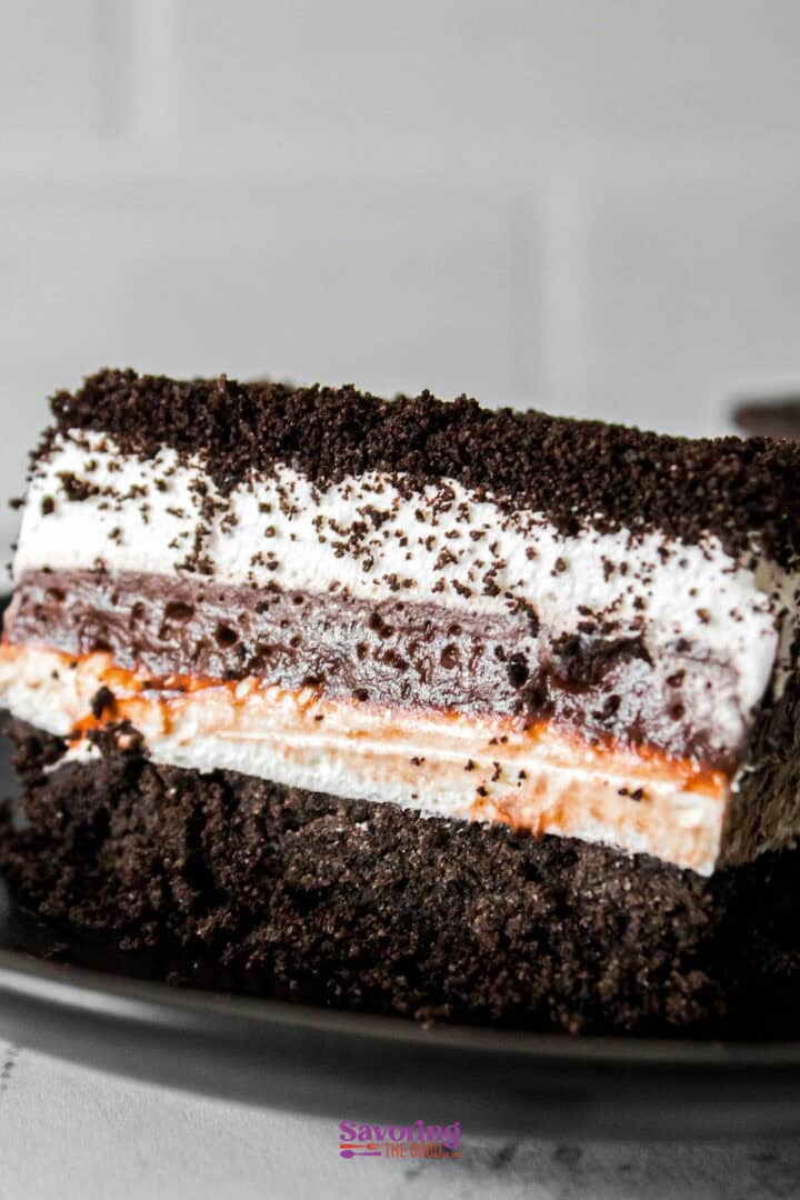 A close-up of a chocolate lasagna dessert reveals crumbly chocolate layers atop a creamy filling, all resting on a rich, dark base, elegantly served on a black plate.