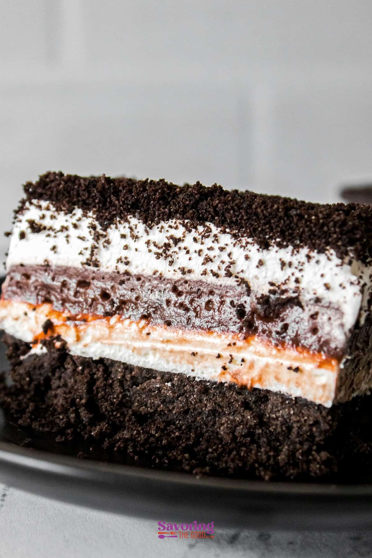 A close-up of a chocolate lasagna dessert reveals crumbly chocolate layers atop a creamy filling, all resting on a rich, dark base, elegantly served on a black plate.