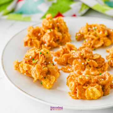 Six delightful cornflake candy clusters with sprinkles rest on a pristine white plate.