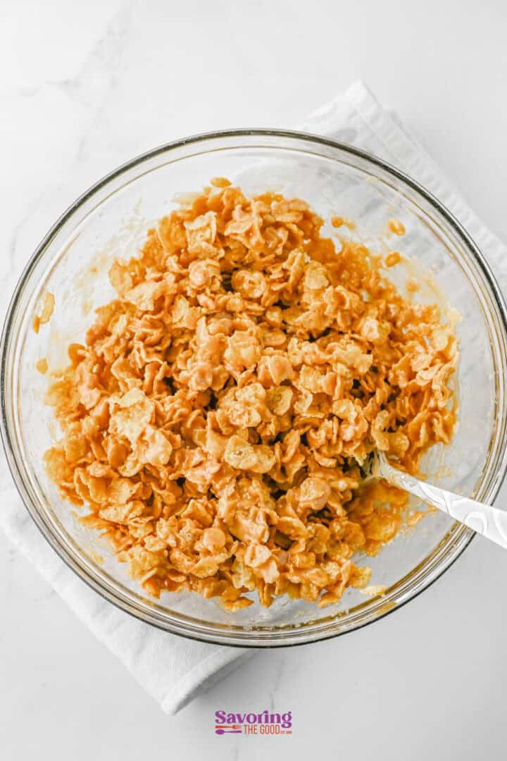 A bowl filled with a delightful blend of cornflakes and a creamy, orange sauce, resembling the sweetness of cornflake candy, with a spoon resting inside.