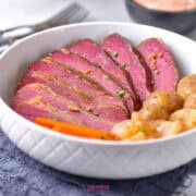 A bowl of Crock Pot Corned Beef with baby potatoes, cabbage, and carrots, garnished with mustard seeds, promises a comforting meal.