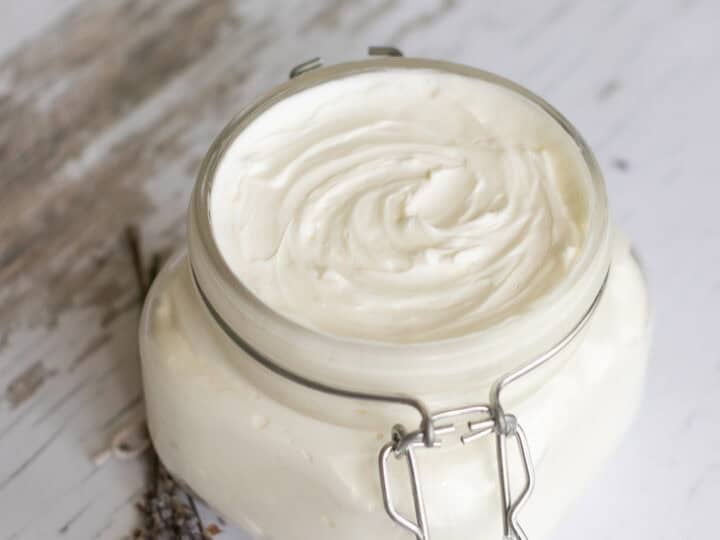 A glass jar filled with white cream, next to sprigs of lavender on a wooden surface.