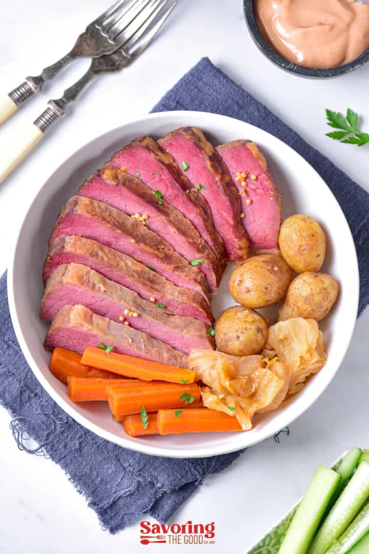 A bowl with sliced rare beef, baby potatoes, cooked carrots, and cabbage. Forks and a dipping sauce are on the side.