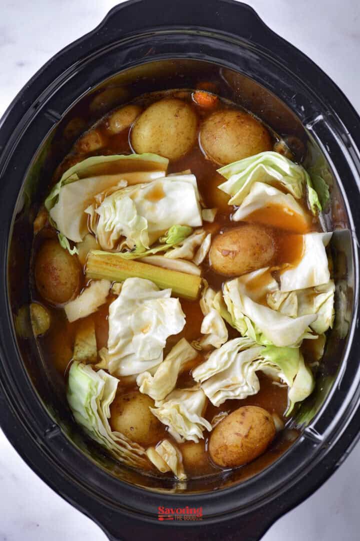 A slow cooker filled with cabbage, potatoes, and other vegetables in a broth.
