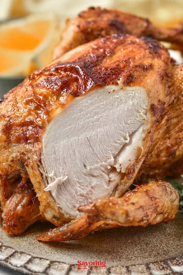 Close-up of a sliced air fryer chicken breast with crispy skin, on a plate with orange slices in the background.