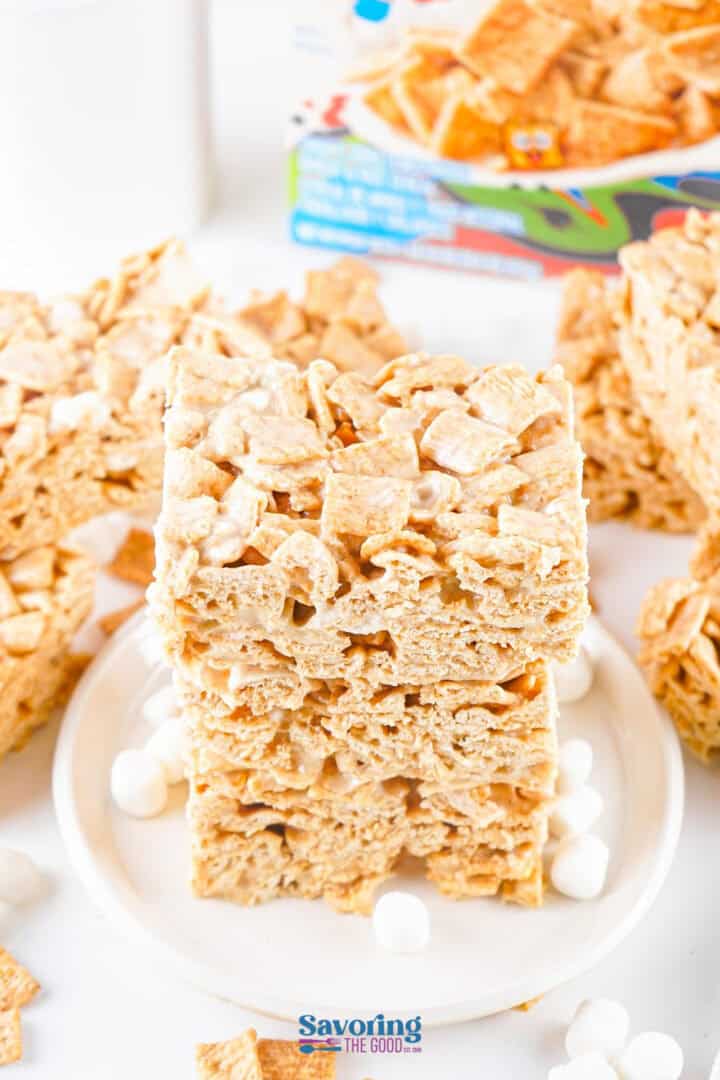 A stack of Cinnamon Toast Crunch Bars and marshmallow treats sit invitingly on a white plate, surrounded by scattered, fluffy marshmallows.