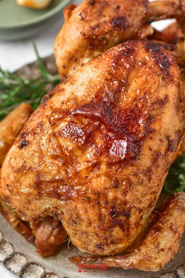 Close-up of a golden-brown air fryer chicken on a platter, garnished with fresh herbs.