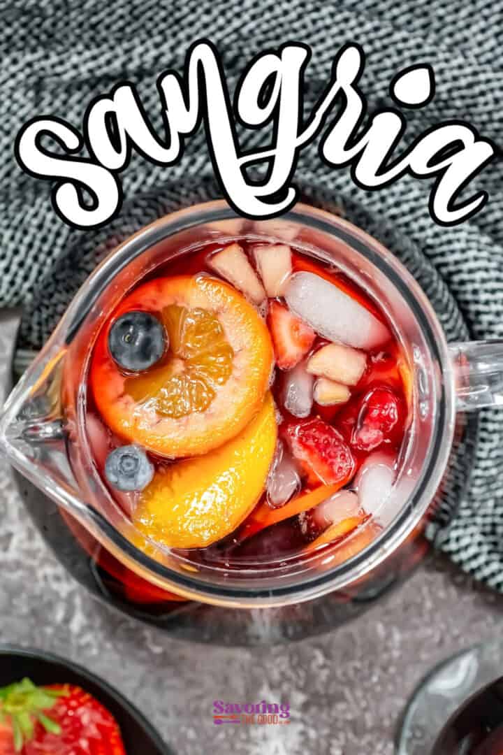 A pitcher of sangria with ice, orange slices, berries, and diced fruit, placed on a textured surface.