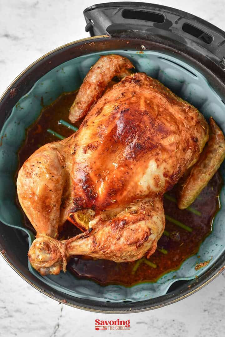 A roasted chicken with a glazed brown surface, cooked to perfection in an air fryer, sits invitingly in a round pan against a white background.
