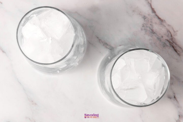 Two glasses filled with ice cubes on a marbled surface.