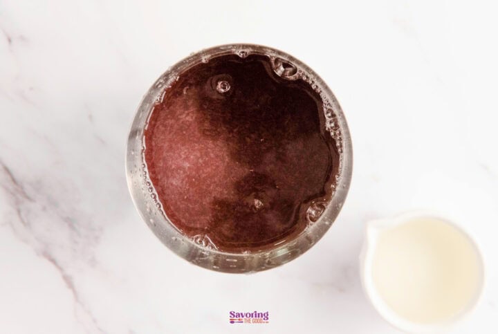 Top view of a glass filled with a dark beverage on a white marble surface, accompanied by a small white pitcher.