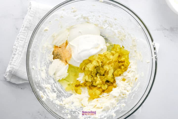 Glass bowl with fried dill pickle dip made from cream cheese, sour cream, chopped pickles, and spices on a marble surface.