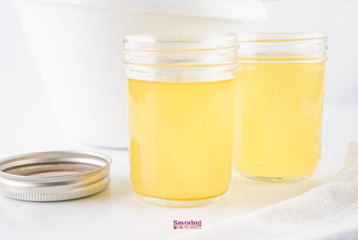 Two glass jars filled with liquid tarrow stand on a white surface, with a metal lid placed nearby.