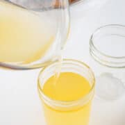 Pouring liquid beef tallow into a glass jar from a measuring cup.