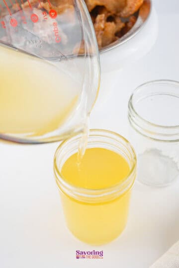 Pouring liquid beef tallow into a glass jar from a measuring cup.