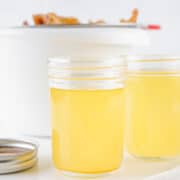 Two jars of clear beef tallow, sit on a white surface, with a pot in the background.