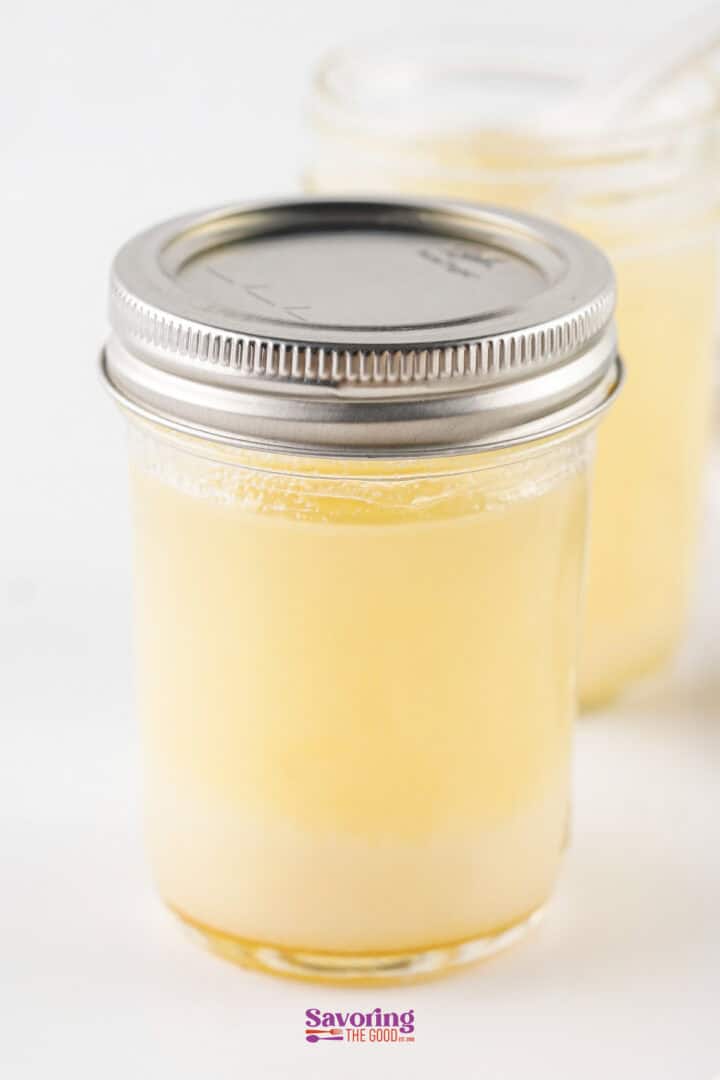 A glass jar with a metal lid containing beef tallow, sits on a white surface. Another jar is partially visible in the background.