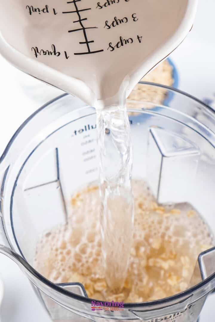 Pouring water into a blender filled with oats.