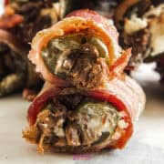 Close-up of Texas Twinkies—bacon-wrapped jalapeños stuffed with cream cheese and shredded meat—stacked invitingly on a plate.
