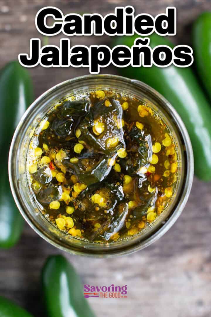 A jar filled with candied jalapeños, surrounded by fresh jalapeños on a wooden surface.