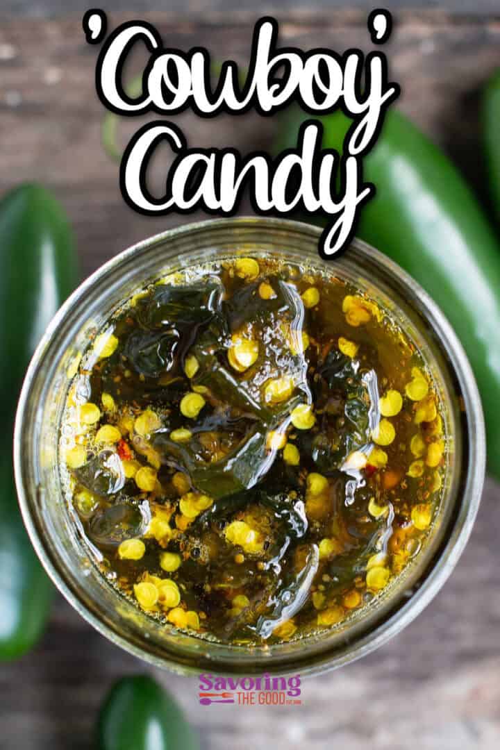 A jar of homemade pickled jalapeños labeled "Cowboy Candy," surrounded by fresh jalapeños on a wooden surface.