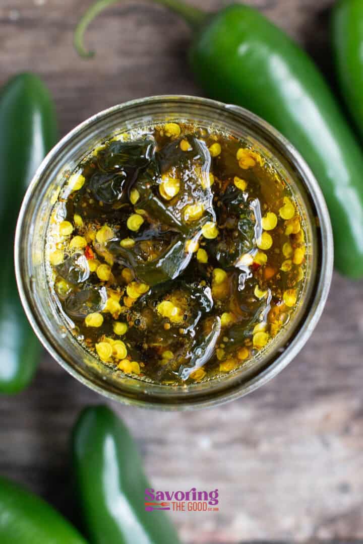 Top view of a jar filled with jalapeño jelly, surrounded by whole jalapeños on a wooden surface.