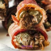 Close-up of Texas Twinkies-bacon-wrapped jalapeño poppers stuffed with savory beef and creamy cheese-resting on a white surface.