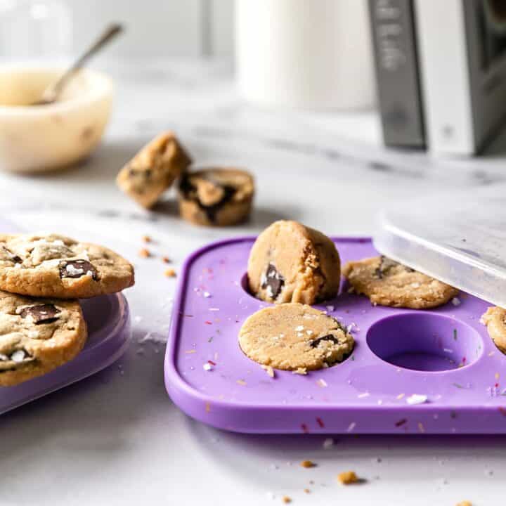 Chocolate chip cookie dough and freshly baked cookies rest on a purple Souper Cube, with a spoon in a bowl and a milk carton in the background.