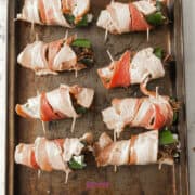 Texas Twinkies: Jalapeños stuffed with cheese and wrapped in bacon, secured with toothpicks on a baking sheet, ready for cooking.