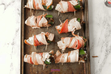 Texas Twinkies: Jalapeños stuffed with cheese and wrapped in bacon, secured with toothpicks on a baking sheet, ready for cooking.