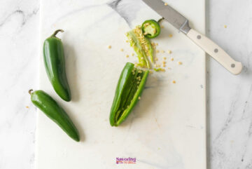 Three jalapeños on a cutting board, one sliced open with seeds exposed and a knife nearby.