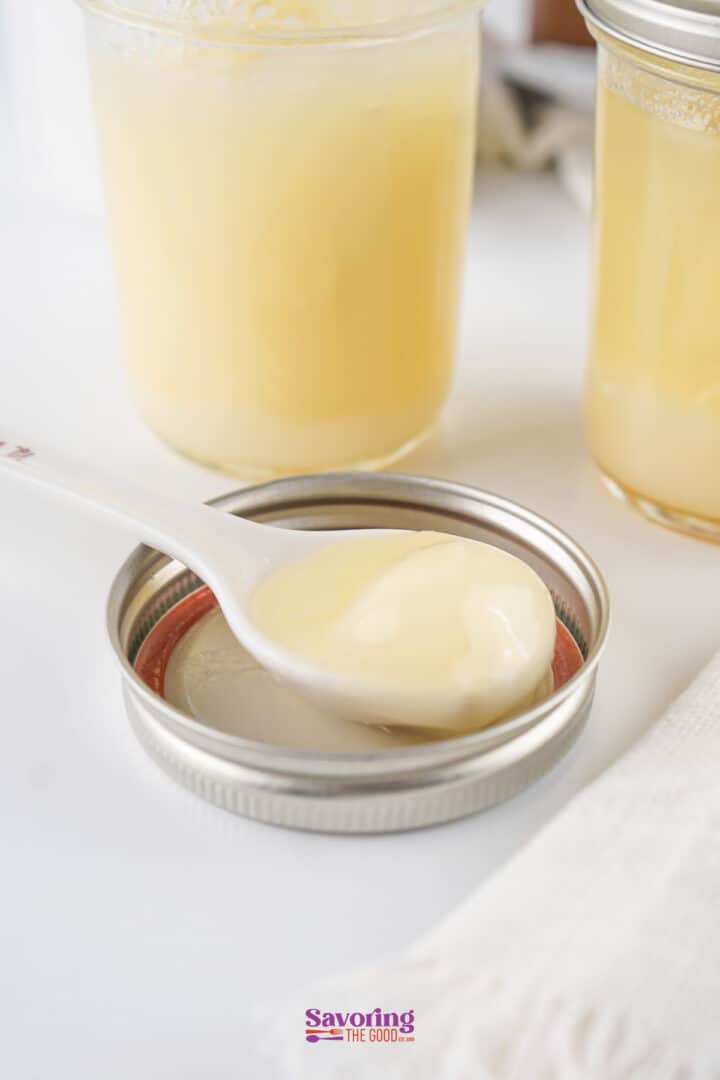 A spoonful of creamy lemon curd rests on a jar lid, with two jars of lemon curd in the background.