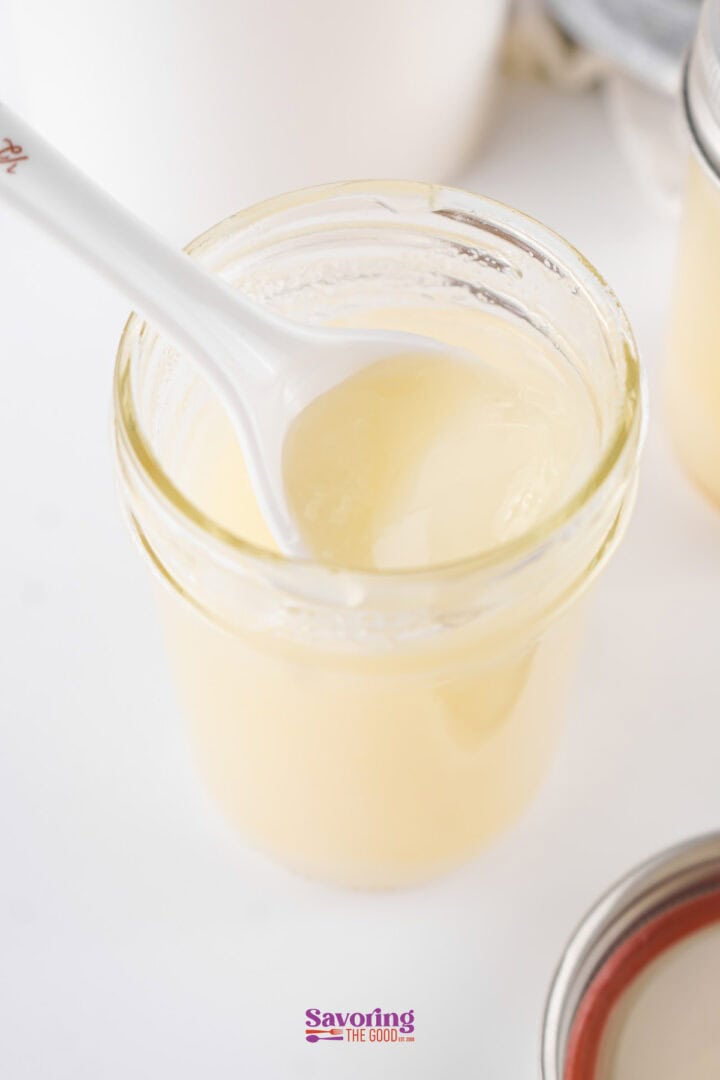 Glass jar filled with creamy yellow condensed milk, shown with a white spoon.