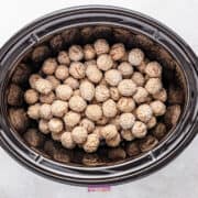 A slow cooker brimming with uncooked, breaded French onion meatballs rests invitingly on a pristine white surface.