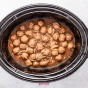 A crockpot brimming with French onion meatballs, bathed in a savory brown sauce and mingling with tender sliced onions.