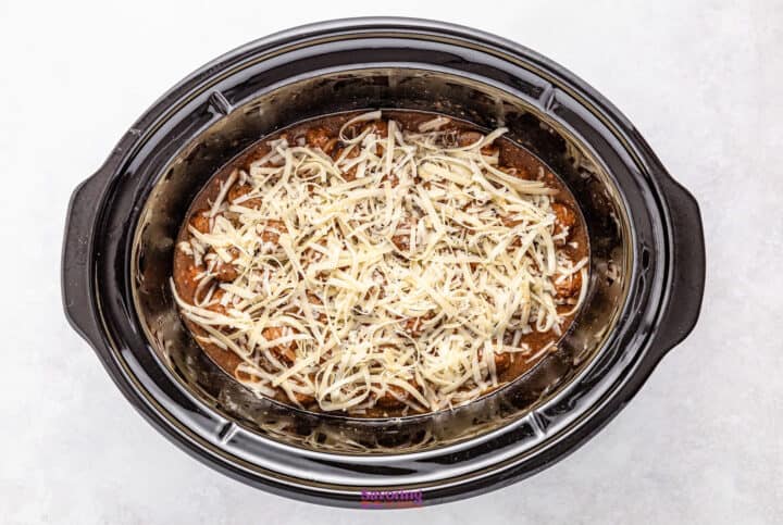 In a cozy crockpot, French onion meatballs nestle under a blanket of shredded cheese, creating an inviting view from above.