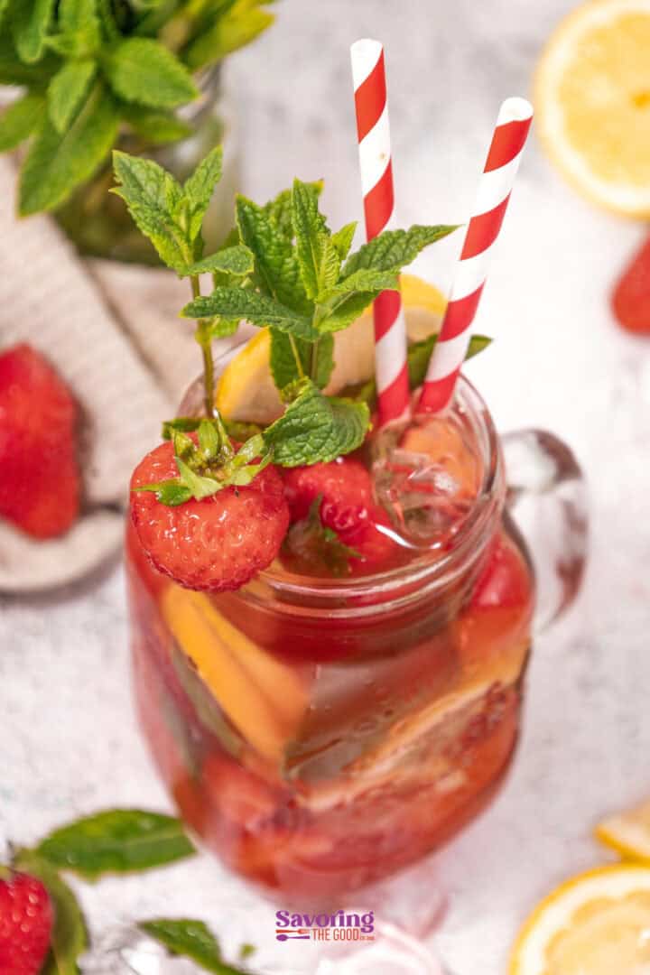 A mason jar filled with a refreshing mocktail with strawberries and citrus, garnished with mint and a strawberry. Two red and white striped straws are inserted, promising a delightful sip.