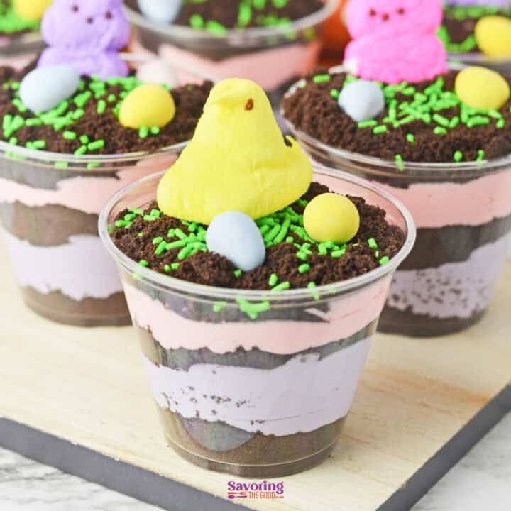Easter dirt cups feature layered dessert with chocolate crumbs, pink and purple cream, and a festive topping of green sprinkles, candy eggs, and yellow marshmallow chicks.
