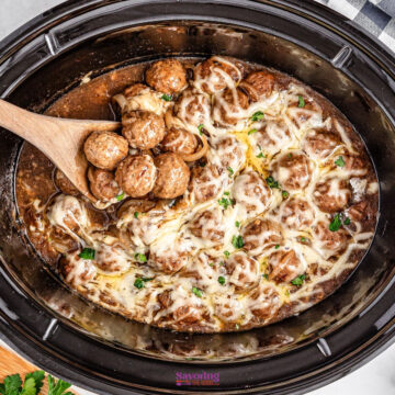 Crockpot meatballs drenched in melted cheese and infused with the rich flavor of French onion soup, a wooden spoon lifting some out.