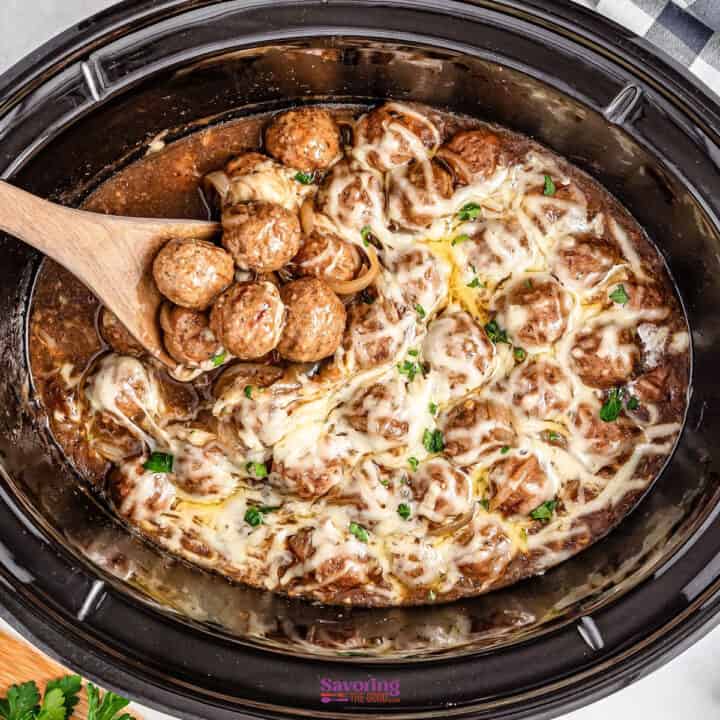 Crockpot meatballs drenched in melted cheese and infused with the rich flavor of French onion soup, a wooden spoon lifting some out.