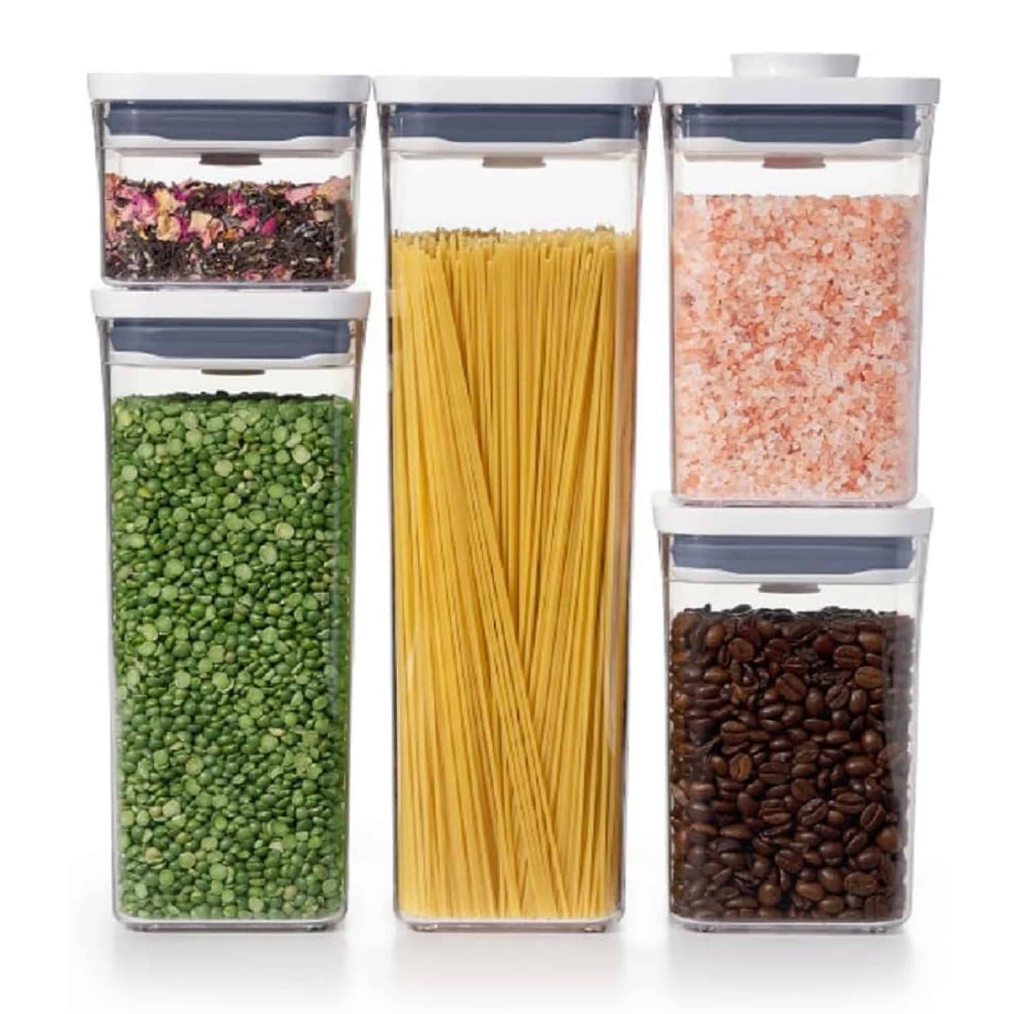 Five clear containers hold rose petal tea, split peas, spaghetti, pink salt, and coffee beans, arranged in two rows against a white background.